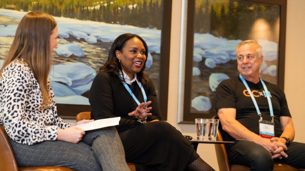 Three people sit in chairs talking in front of an audience