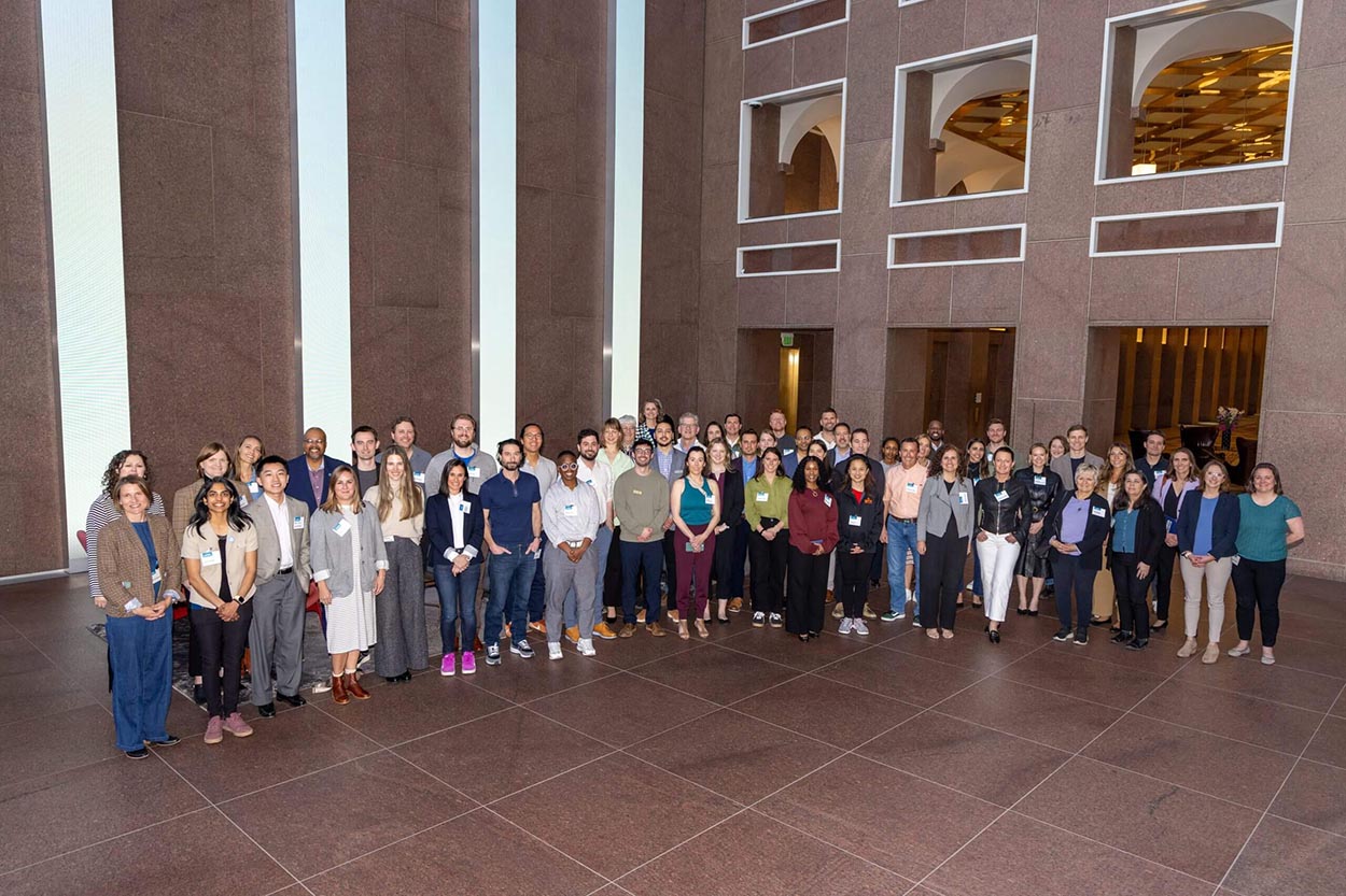 A group of 60 people in business dress pose in a large indoor lobby.