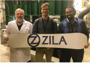 Three men pose with a Zila-branded snowboard prototype